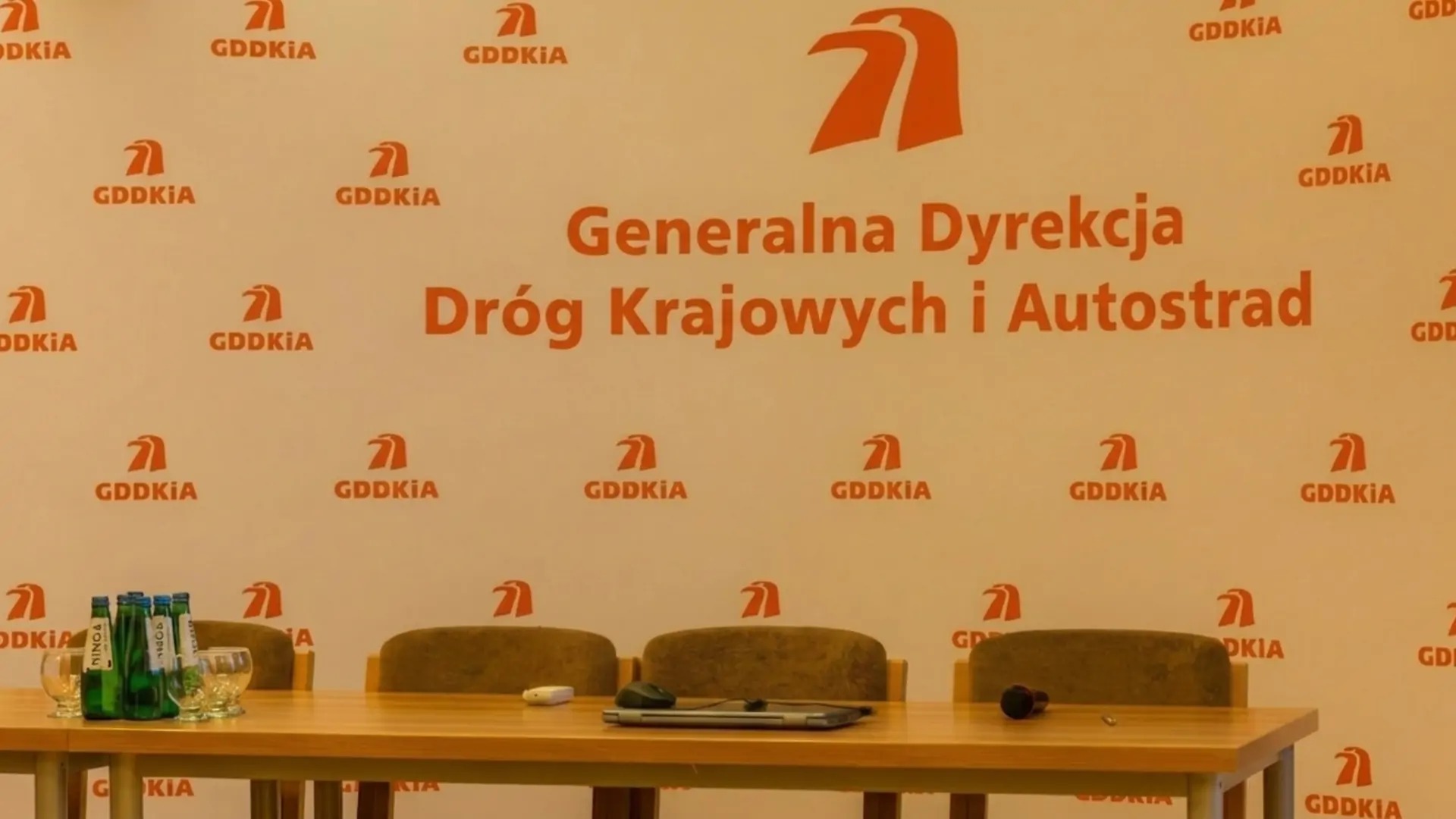 Ścianka z logo GDDKiA. Przed ścianką stół i krzesła.
